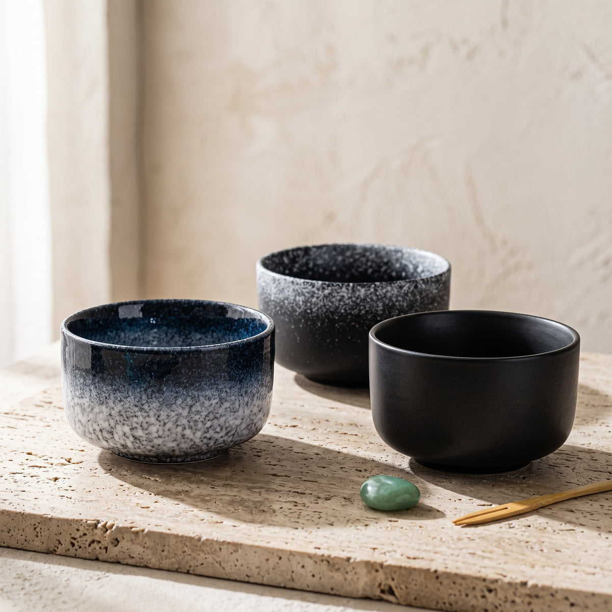 Les trois bols matcha chawan Sumi réunis sur une pierre de travertin, finitions Brume, Encre et Suie — Aoti Matcha
